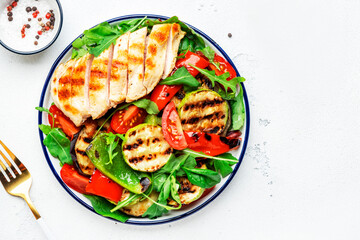 Healthy salad with grilled chicken breast fillet and vegetables: paprika, zucchini, eggplant, fresh tomatoes and mixed herbs. White table background, top view