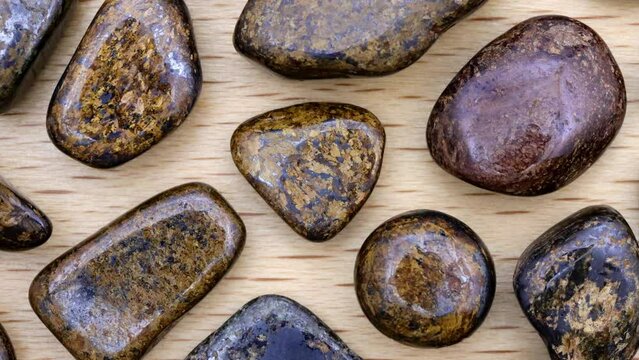 Bronzite rare jewel stones texture on light varnished wood background. Moving right seamless loop backdrop.