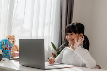 Asian schoolgirl doing her homework with laptop at home. Children use gadgets to study. Education and distance learning for kids. Homeschooling during quarantine. Stay at home