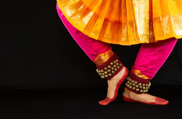Feet of female Indian Bharatanatyam classical dancer in traditional costume in dark background. 