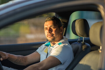 Aboriginal man seen through passenger window driving a car with dark interior