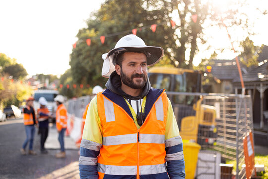man road worker with beard wearing white hat with yellow and orange high-vis jacket doing roadwork