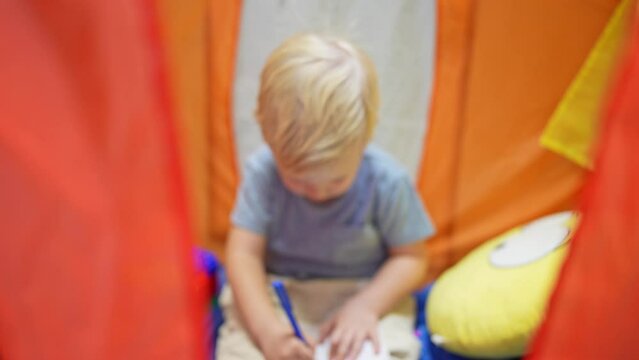 Portrait of a thoughtful little boy writing a letter to Santa Claus before Christmas in a children's house tent. The concept of the New Year and holidays