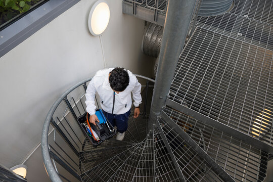 Young male technician carrying tool box on stairs
