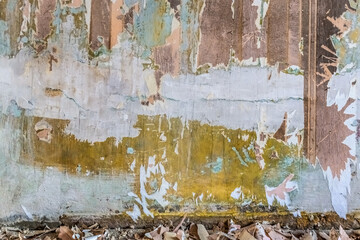 Pieces of paper torn wallpaper lie on the floor against an old shabby wall with layers of paint and plaster. Building architectural background with copy space