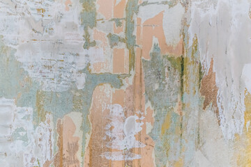 Light pink-blue-gray pastel vintage texture of shabby scratched old cement wall. Pieces of peeled wallpaper among colored layers of paint and putty. Real abstract pattern