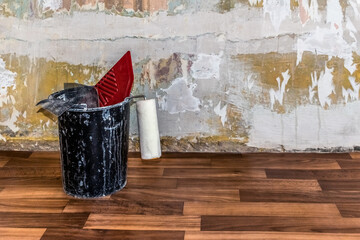 Bucket with a roller for paint, a smoothing wallpaper spatula and an abrasive mesh stands on a...