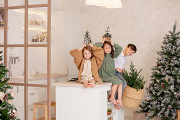 Three children - two girls and a boy, happy together at home in the kitchen preparing Christmas dinner at the Christmas tree