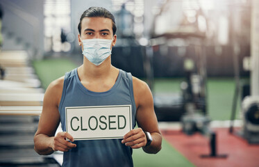 Covid, gym and man holding closed sign during the pandemic while wearing a face mask. Coronavirus, health center and quarantine lockdown with fit, strong male in empty gymnasium