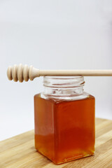 Sweet honey in a jar with a stick on a wooden board