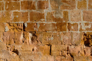 close-up of a limestone masonry wall, yellowish, orange, of a medieval hermitage in Burgos Spain, eroded by the wind, by the blows from the rest of the shots and the impact of projectiles in the war, 