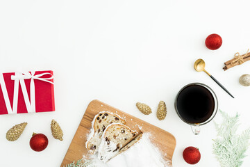 Christmas composition with stollen cake on a wooden board with coffee cup, toys and gift box on white. Flat lay