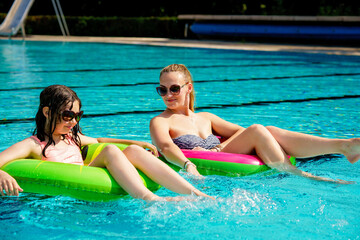 Happy little girl and young mother playing with colorful inflatable rings in outdoor swimming pool on sunny summer day. school child and mum relax. Summer family outdoor activity