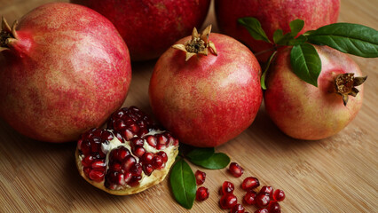 Several ripe pomegranate fruits and an open pomegranate with pomegranate leaves on a wooden old cutting board, side view.