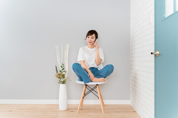 家で椅子に座りながらスマホを使うアジア人女性  © buritora