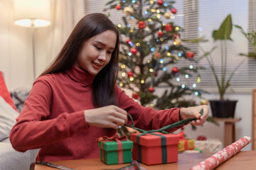 Obraz na płótnie Canvas Young beautiful Asian woman prepare and wrap Christmas present gift box for send to family friend or boyfriend during Christmas festival celebration at home, Merry Christmas and happy new year concept