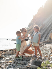 Little siblings helping mother to collect garbage on sea beach in plastic bag. Happy family activists collecting trash. Concept about environmental conservation pollution problems and responsibility.