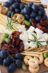 Cheese plate served with grapes, olives, crackers and dried tomatoes on a wooden background, selective focus