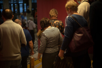 People are walking inside building. Lot of people leave room. Old people after concert.