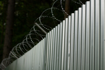 Steel fence with barbed wire. Fence around plant. Private territory. Metal profile. Dangerous wire.