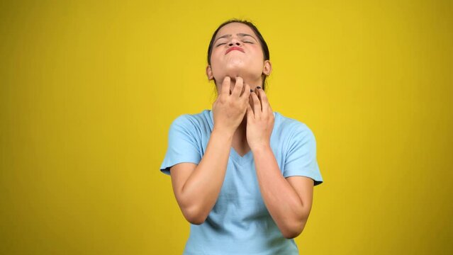Young woman scratching neck on yellow background, girl itching her neck annoyed