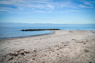 Sandy beach on the coast of Denmark. Stone groyne in the bay, sunshine while walking