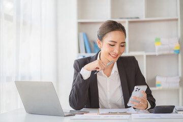 Obraz premium Young beautiful asian woman using smartphone and working with laptop while sitting at office desk, working from home concept.