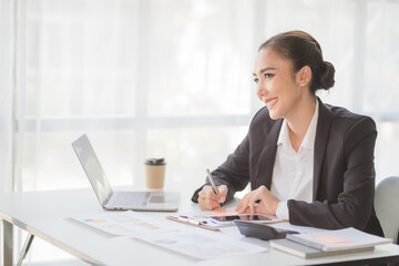 Portrait of beautiful smiling young entrepreneur businesswoman holding cup of coffee and working on laptop computer at office. Panoramic background.