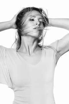 Portrait of beautiful and sexy looking woman with bright tight dress in white background. Model standing with raised hand behind her head and her face covered with spinning hair. Black and white image