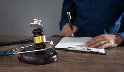 Fototapeta na wymiar Man signing in document. Judge gavel and stethoscope on the table