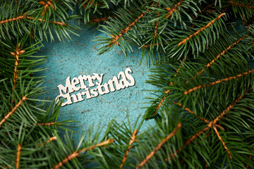 Inscription of Merry christmas on a blue paper background surrounded by fir branches