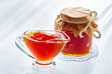 Sweet orange color fruit jam in a glass gravy boat and in a jar on a light morning background