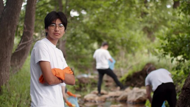 Asian eco volunteer young man stands with people on background collecting garbage in nature. The concept of care and protect the environment from human influence.