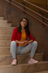 Latin young woman in jeans sitting defiantly on a stair step in an industrial interior