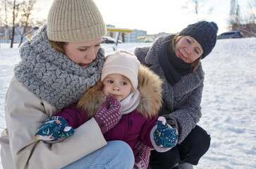 Fototapeta premium Grandmother, mother and daughter are walking in the winter city park on Christmas and New Year holidays. Parent and little child having fun outdoors
