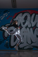 Silhouette of young woman hip-hop dancer (break-dancer)dancing on graffiti studio background. Contrast colors.