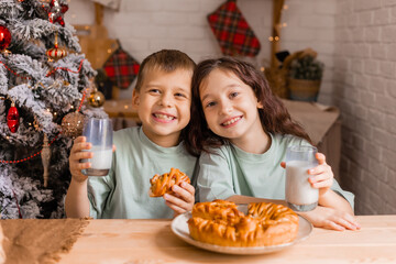 two small children a boy and a girl eat Christmas cake with milk in the morning at home in the kitchen