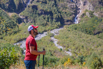 A hiker with canes looks into the distance on a path in the mountains to the waterfalls.