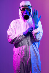 Coronavirus covid-19 pandemic. Doctor scientist wearing protective biological suit and mask due to global healthcare epidemic warning and danger background in blue and pink neon lights background.