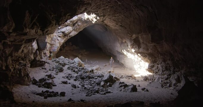 Man walks through light of giant cave and stands on caved in rocks wide