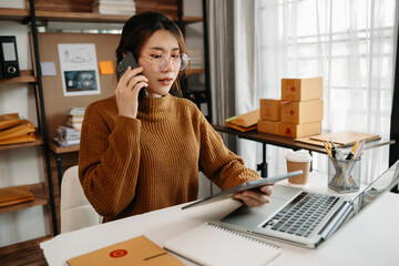 Portrait of Asian young woman SME working using smartphone or tablet taking receive and checking...