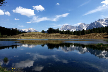 Alp mountains reflecting at a lonesome lake with blue cloudy sky