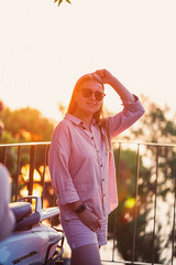 A beautiful woman at sunset stands on a terrace overlooking the sea.