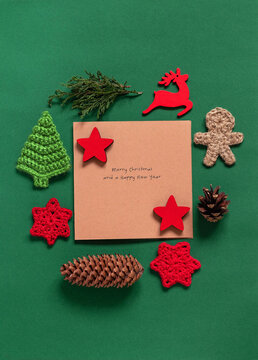 Christmas greeting card, crochet tree toys, wooden toys, cypres branches and cones on a green backgorund. Copy space. Top view.
