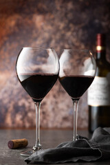 Glasses of red wine with bottle nearby on dark background