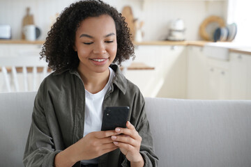 Fototapeta na wymiar Happy mixed race teen girl holding smartphone uses mobile apps, chatting or shopping online at home