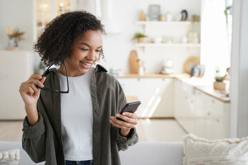 Smiling young mixed race girl using mobile apps, holding phone, shopping in online store at home