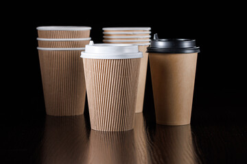 Several disposable paper cups with lids of different types and sizes for drinks on a black...