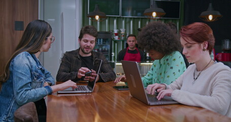 Fototapeta premium People using devices at coffee shop interior. Group of work colleagues working remotely at cafe restaurant in front of laptop computers