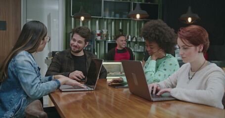 Fototapeta premium Group of people seated at coffee shop in front of laptop computers. Young millennials working or studying remotely using modern technology devices